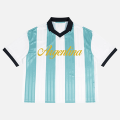 A short-sleeve Argentina soccer jersey with vertical light blue and white stripes, a black V-neck collar, black sleeve trim, and 'Argentina' printed in gold script across the chest, shown on a plain white background.