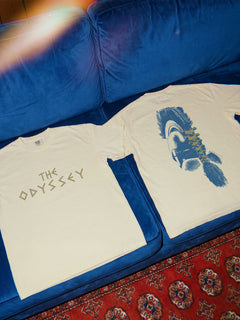 beige Comfort COlors The Odyssey 2026 movie t-shirt with custom movie poster text logo and soldier helmet with front and back print on a black comfort colors graphic tee